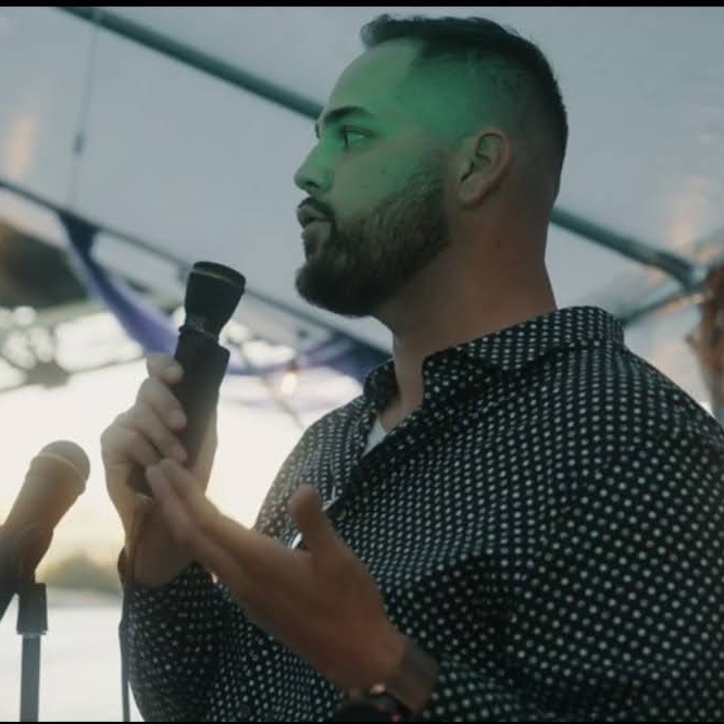 John speaking to a room, holding a microphone.